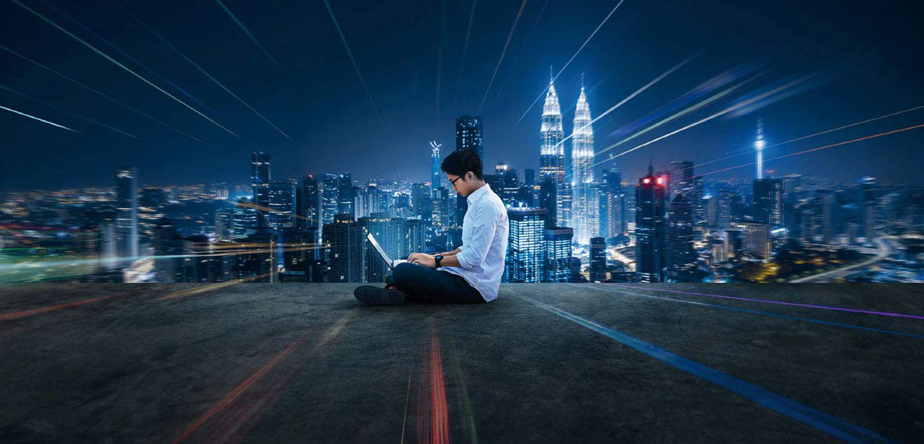 A man sitting on the floor using laptop with Malaysia night view A man sitting on the floor using laptop with Malaysia night view