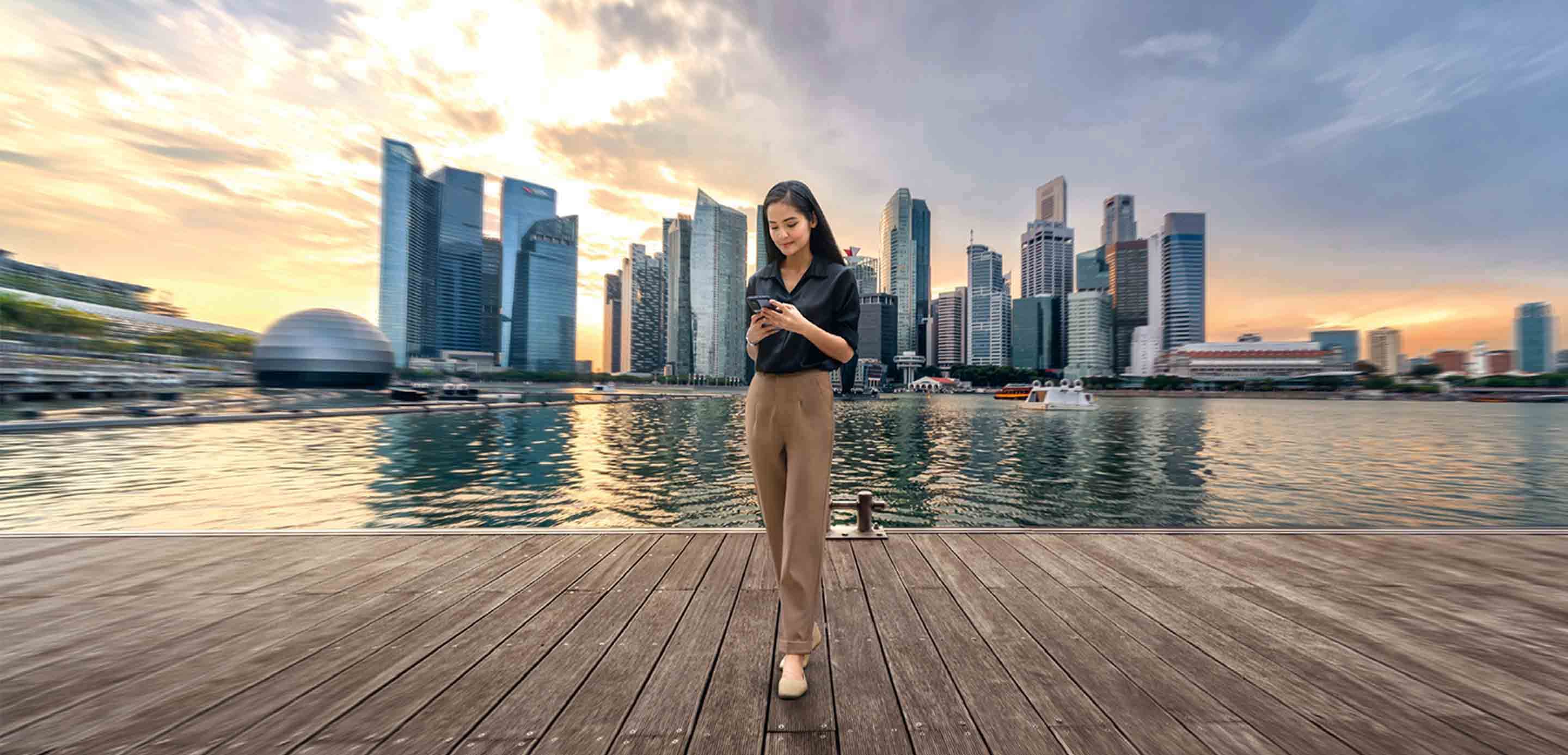 Woman standing at harbour front in Singapore using mobile phone Woman standing at harbour front in Singapore using mobile phone