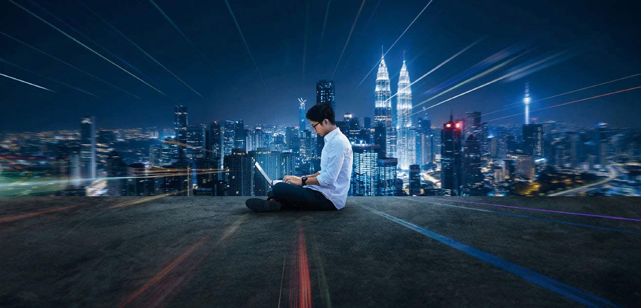 A man sitting on the floor using laptop with Malaysia night view A man sitting on the floor using laptop with Malaysia night view